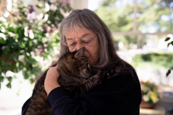 Meals on Wheels client holds her cat close and kisses its head.