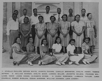 A black and white archival image of a group of pepole standing and sitting posed for the camera