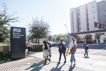 Students walking in front of a sign that reads "ASU Barrett, The Honors College" on ASU's Tempe campus.