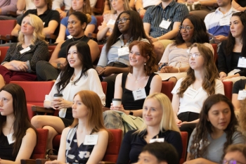 A group of students smiles in an auditorium sitting in red seats.
