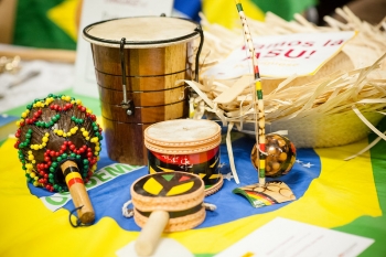 Culturally specific percussive musical instruments cover a table. They are light tan and medium brown in color with red, green and yellow accents.