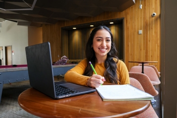 Student seated at a desk with a laptop and a notebook.