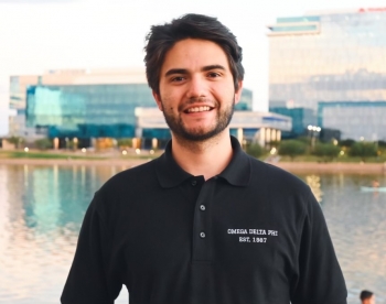 College of Health Solutions graduate Angel Jose Sanchez wearing a polo and standing in front of Tempe Town Lake, looking at the camera and smiling.
