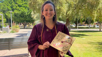 Angie Haskovec smiles at the camera. She's wearing her maroon graduation gown and holding her decorated gold graduation cap. 