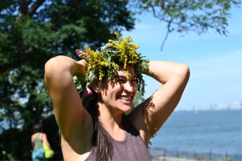 Aly Stoffo wearing a crown of greenery and smiling with her arms raised and a body of water and trees in the background.
