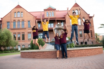 A family of five in maroon and gold celebrates in front of the Old Main fountain