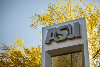 Sign with the letters "ASU" on a campus, surrounded by a tree in bloom.