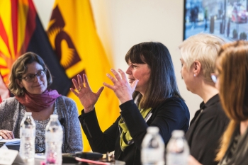 Various faculty engaged in discussion in the foreground with the Arizona state flag and ASU flag in the background. 
