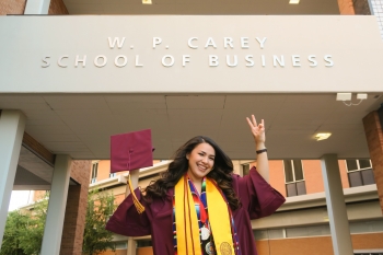 Berenice Pelayo in front of the WP Carey Business School in her cap and gown