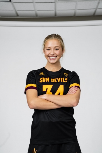 Brynn Holohan posing with arms crossed and smiling in her sports uniform against a white backdrop.