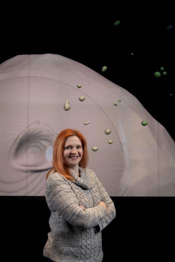ASU alum Wendy Caldwell stands smiling, with arms folded in front of a digital rendering of an asteroid.