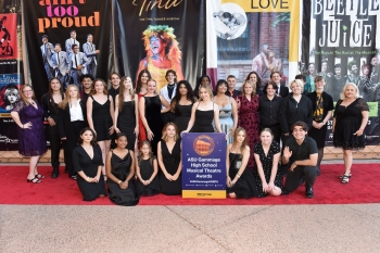 A group of high school students all dressed in black posing for a photo with production signs surrounding them.