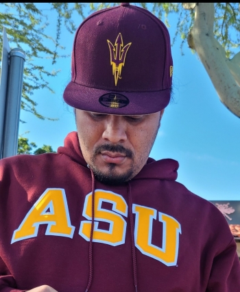 ASU student Cordero Holmes is pictured looking down, wearing an ASU hat and sweatshirt, in an outdoor setting.