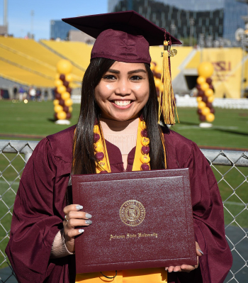 Danni Baquing smiling and posing with ASU degree wearing graduation gown and stole in an outdoor setting with maroon and gold balloons behind her.