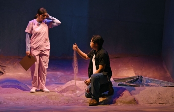 Man kneels with sand flowing through his fingers while a nurse, standing, looks on.
