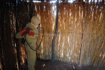 An employee of the National Malaria Control Program in Mozambique spraying insecticides on walls inside a home.