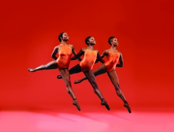 Three ballerinas in orange leotards performing and jumping in unison