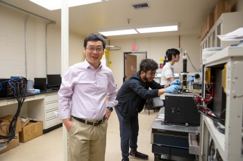 Hongbin Yu poses in front of his students conducting research in his lab in the background.