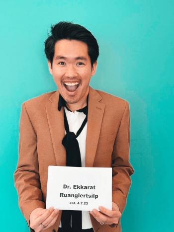 Graduating linguistics PhD student Ekkarat Ruanglertsilp stands against a blue background, smiling and holding a sign celebrating the date he defended his dissertation. / Photo by Demetria Baker