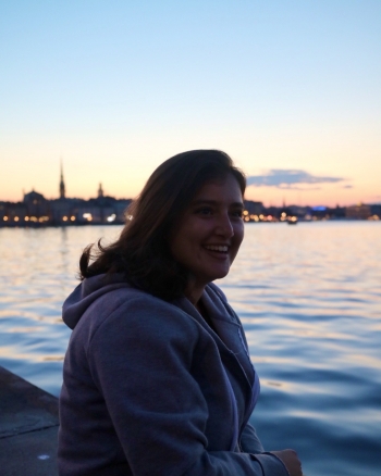Foreign exchange student Elisa Cardamone is seen in front of a body of water. The sun is low on the horizon and a lit-up city skyline is silhouetted in the distance behind her.