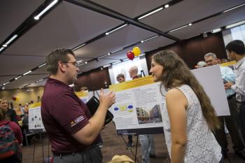 Photo of female student talking with a man in front of a poster with a caption of "Sharing your research and ideas at the FURI Symposium are part of the experience for undergraduate researchers like Emily Ford (right). Photographer: Jessica Hochreiter/ASU