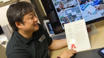 ASU Professor Gail-Joon Ahn pictured holding an award certificate in an office setting.