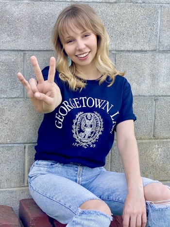 Victoria Stratton smiles wearing a Georgetown Law shirt and holding her fingers in a pitchfork symbol