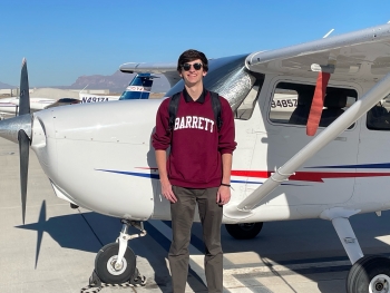 ASU grad Grant Penderghast wearing a maroon sweatshirt that says "Barrett" while standing next to a small airplane.
