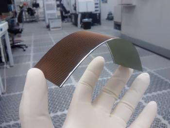 A gloved hand holds a flexible solar cell in a lab.