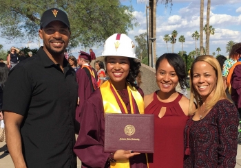 A woman in a graduation gown and construction hat stands with her family at a 2017 ASU graduation
