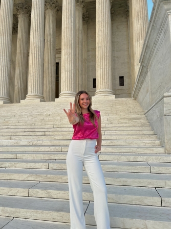 Logan Higgins on the steps of the Supreme Court doing the forks up hand gesture.
