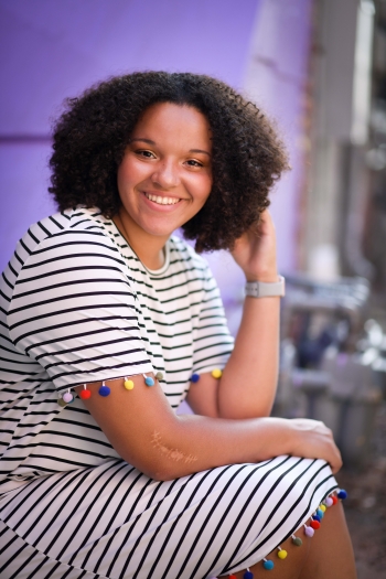 Photo of Jayla Johnson smiling and wearing a striped dress against a partly purple background