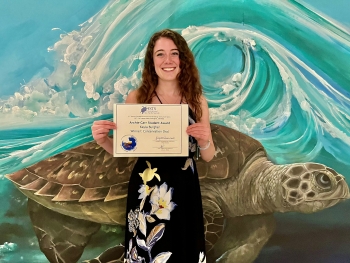 Kayla Burgher holds award in front of a sea turtle mural.