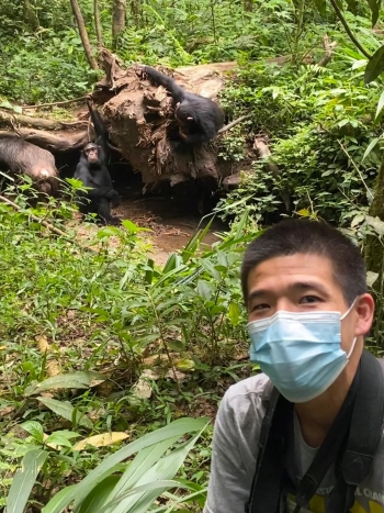 Man taking a selfie in a forest with a chimpanzee in the background.