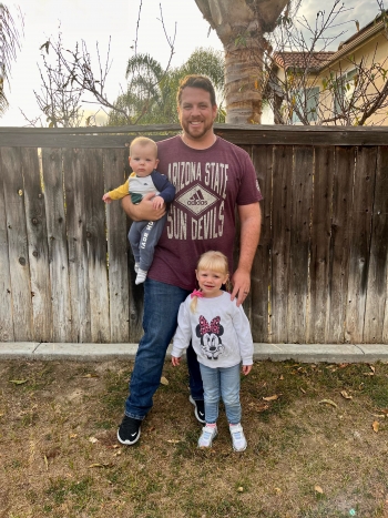 Kyle Durrschmidt, ASU Online graduate, stands with two children in front of an outdoor wooden fence