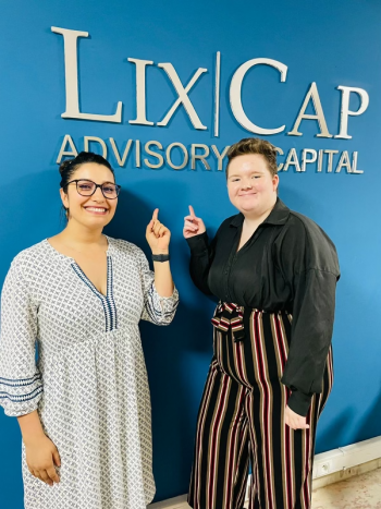 Two people smiling and pointing to a sign on a wall that reads "Lix|Cap Advisory Capital."