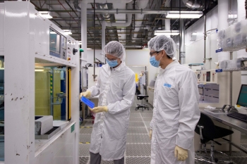 Two people wearing white lab coats and gear while working in a lab.