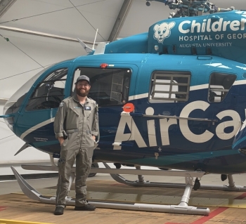 ASU alum Jason Herman stands in his nursing flight suit next to a medical helicopter.