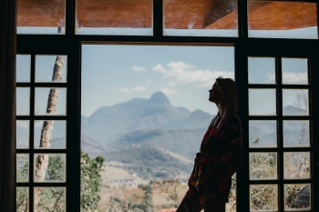 Silhouette of a woman leaning against a doorway. In the background is a mountainous landscape.