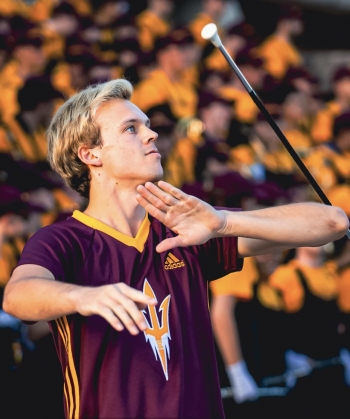 ASU graduating student twirling baton for ASU. Foreground is Cody with baton in action, background is blurred shot of audience in stadium