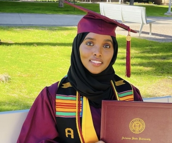 ASU student Maryam Abdulle poses for a photo in a graduation gown and cap, holding her diploma cover
