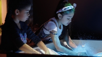 Two young girls use their hands to manipulate an electronic map at the "Mission Future" exhibition, located at the Arizona Science Center