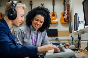 Student wearing headphones playing a keyboard as an instructor watches.