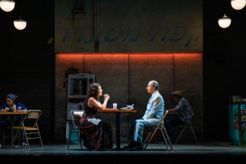 A man and a woman are seated at a table on a stage.