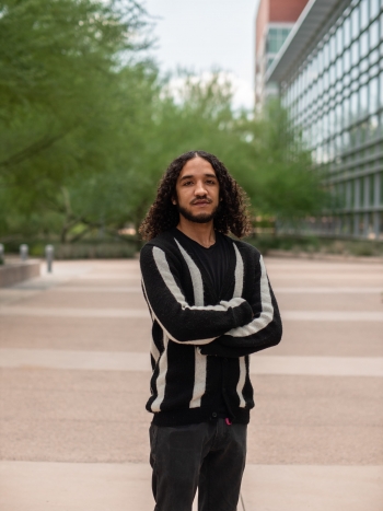 ASU graduate student Dylan Peay stands with arms crossed in the middle of a mall on the Tempe campus