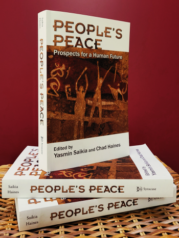 “People’s Peace: Prospects for a Human Future" books stacked on wicker surface, with dark red background. Book cover is white with title and image of primitive artwork of people in motion.