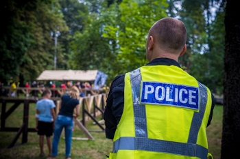 Man wearing a bright vest that reads "police" seen from behind looking toward people at an event.