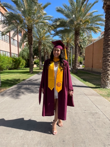 ASU graduate Sami Shah wearing a maroon graduation cap and gown surrounded by palm trees on the Tempe campus.