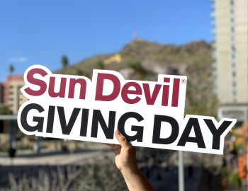 A cutout sign that reads, "Sun Devil Giving Day" is held up in front of Tempe's "A" Mountain in the background.