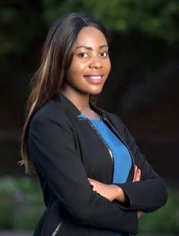 Portrait of ASU grad Shantel Marekera. She has long dark hair and wears a black blazer over a blue shirt with her arms crossed while smiling at the camera.